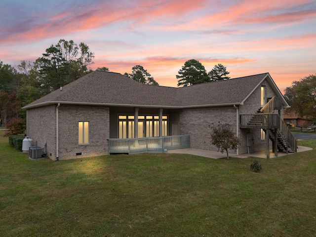 back house at dusk with central AC, a lawn, and a patio