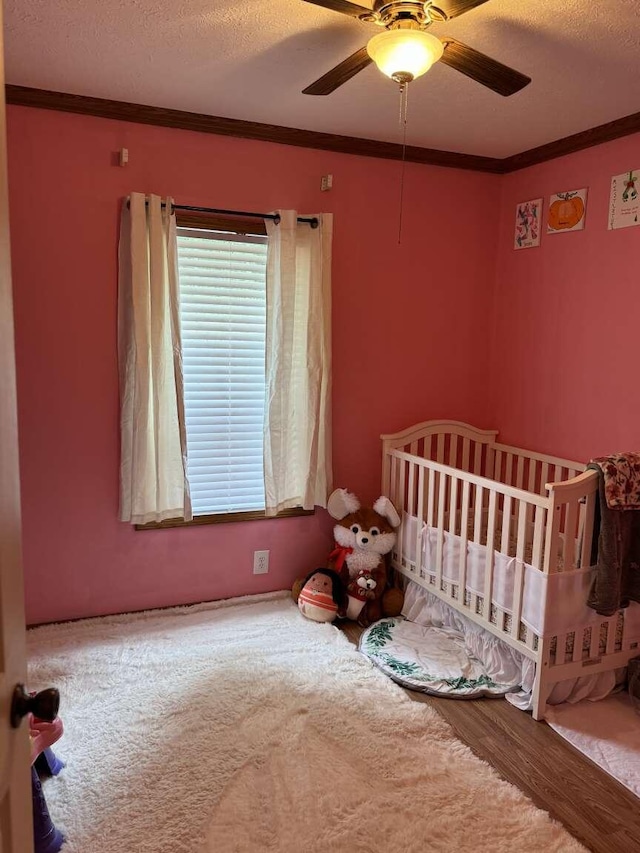 carpeted bedroom featuring ceiling fan, a textured ceiling, a nursery area, and ornamental molding