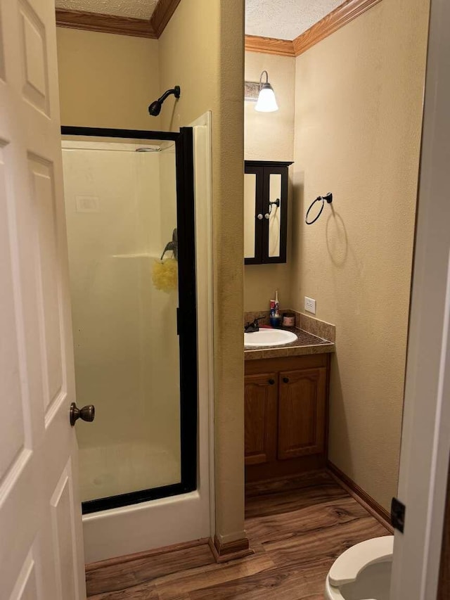 bathroom with vanity, wood finished floors, a stall shower, crown molding, and toilet