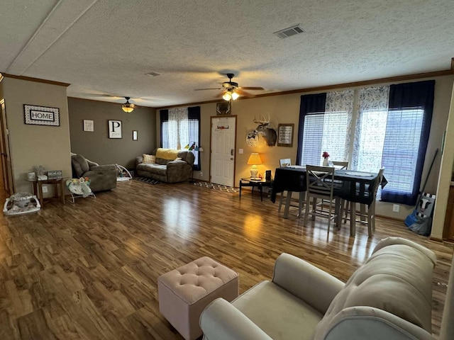 living room with visible vents, wood finished floors, ceiling fan, and ornamental molding