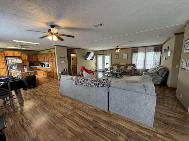 living area featuring visible vents, ornamental molding, a textured ceiling, dark wood finished floors, and ceiling fan