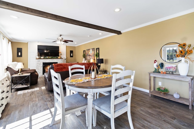 dining space featuring a fireplace, crown molding, beamed ceiling, dark wood-type flooring, and ceiling fan