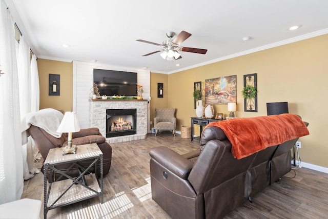 living room featuring ceiling fan, ornamental molding, a stone fireplace, and wood-type flooring