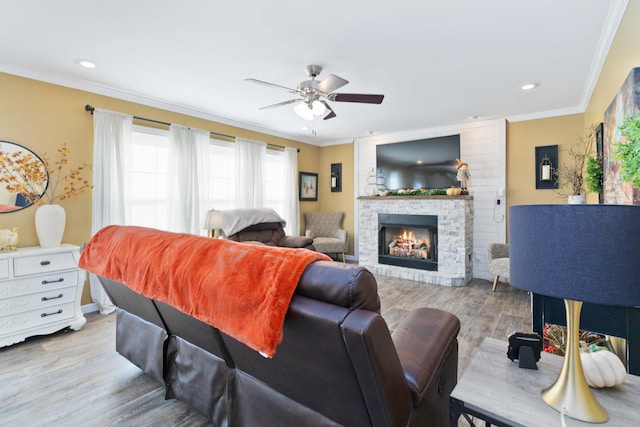 living room featuring a fireplace, crown molding, light hardwood / wood-style flooring, and ceiling fan