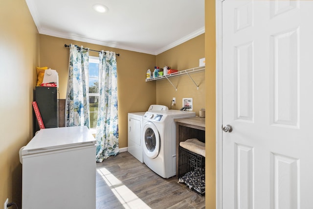 clothes washing area featuring hardwood / wood-style flooring, crown molding, and separate washer and dryer