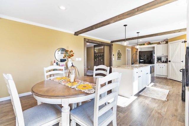 dining room featuring light hardwood / wood-style flooring, beam ceiling, crown molding, sink, and a barn door