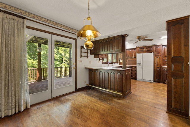 kitchen featuring pendant lighting, hardwood / wood-style flooring, dark brown cabinets, white fridge with ice dispenser, and kitchen peninsula