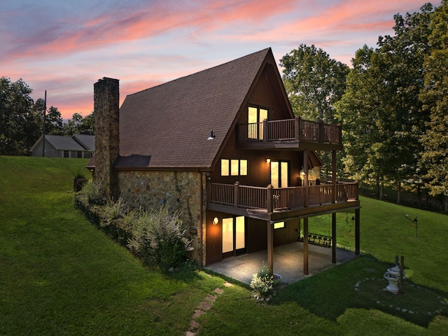 back house at dusk with a yard, a deck, and a patio area