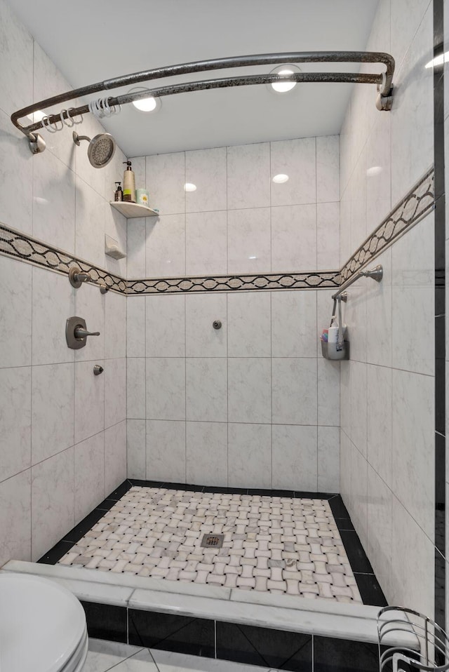 bathroom featuring toilet, tile patterned flooring, and a tile shower