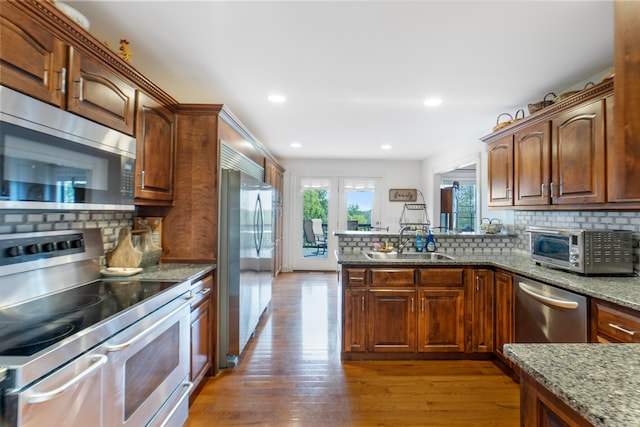 kitchen featuring light stone countertops, light hardwood / wood-style flooring, appliances with stainless steel finishes, sink, and decorative backsplash