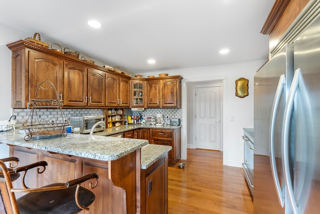 kitchen featuring tasteful backsplash, light hardwood / wood-style floors, kitchen peninsula, stainless steel refrigerator, and light stone counters