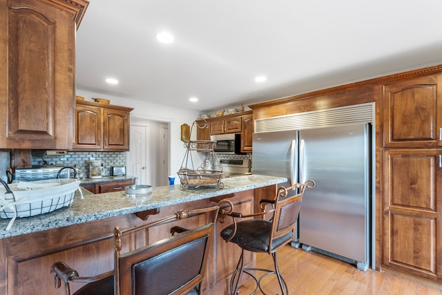 kitchen with light stone countertops, light hardwood / wood-style floors, a kitchen bar, stainless steel appliances, and decorative backsplash