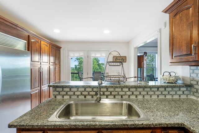 kitchen with a healthy amount of sunlight, dark stone countertops, decorative backsplash, and stainless steel built in refrigerator