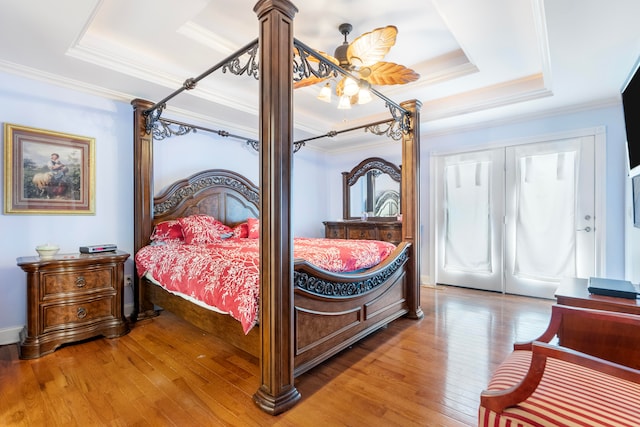 bedroom with ornamental molding, ceiling fan with notable chandelier, wood-type flooring, and a tray ceiling