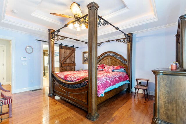 bedroom featuring hardwood / wood-style floors, connected bathroom, ceiling fan, a tray ceiling, and a barn door