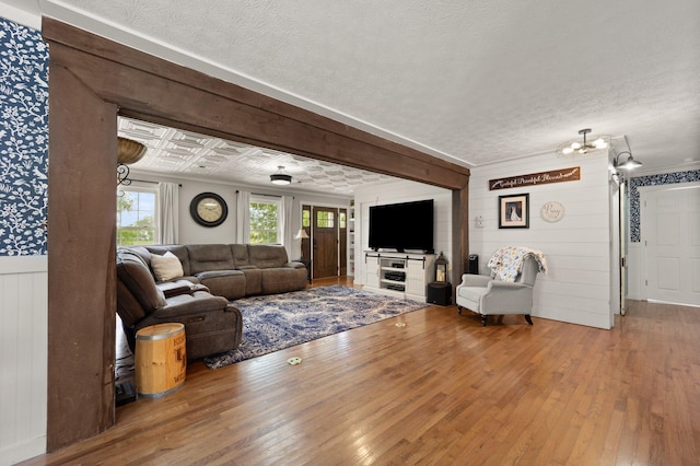 living room featuring a textured ceiling, hardwood / wood-style floors, wooden walls, and beamed ceiling