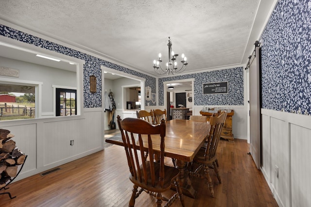 dining room with crown molding, a barn door, hardwood / wood-style floors, a chandelier, and a textured ceiling