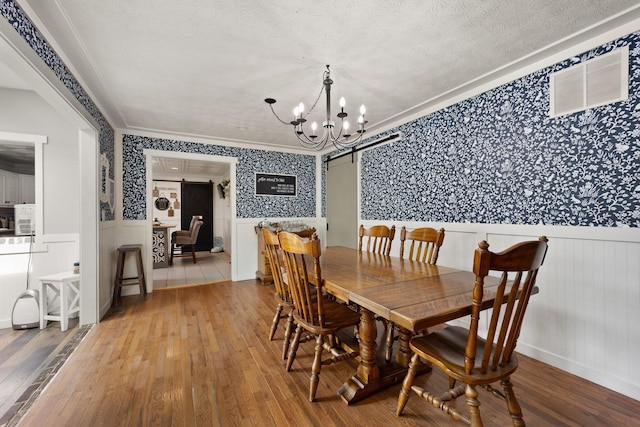 dining space with a textured ceiling, ornamental molding, wood-type flooring, and a notable chandelier