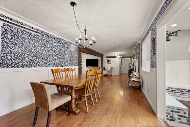 dining area featuring a textured ceiling, ornamental molding, an inviting chandelier, and light hardwood / wood-style floors