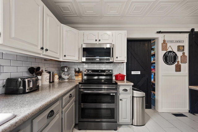 kitchen featuring a barn door, appliances with stainless steel finishes, and white cabinetry