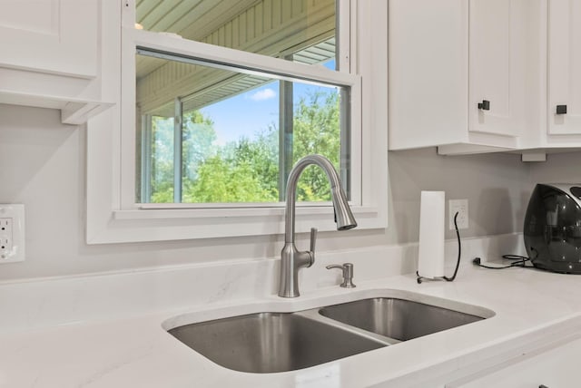 interior details featuring white cabinetry, sink, and light stone countertops