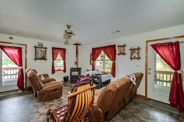 living room featuring a textured ceiling, ceiling fan, and a wood stove