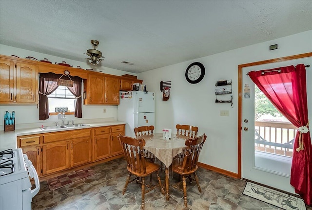 kitchen with a textured ceiling, white appliances, sink, and ceiling fan