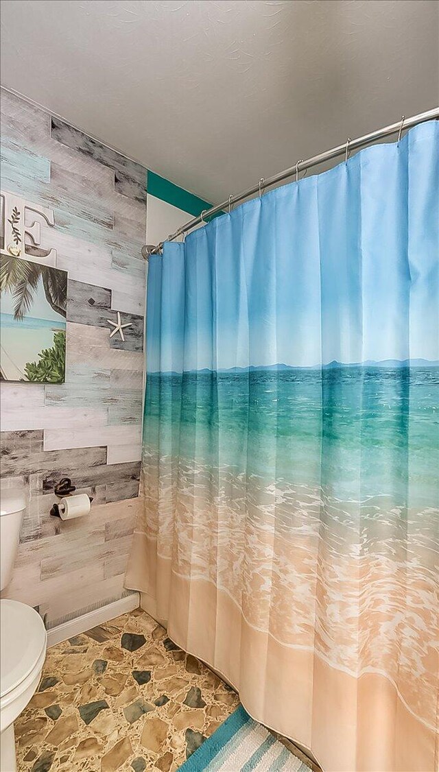 bathroom featuring wooden walls, toilet, and a shower with curtain