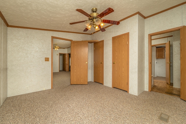 unfurnished bedroom featuring a textured ceiling, light carpet, ornamental molding, two closets, and ceiling fan