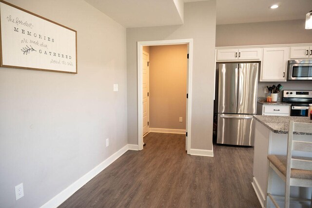 kitchen featuring appliances with stainless steel finishes, light stone counters, white cabinets, and dark hardwood / wood-style floors