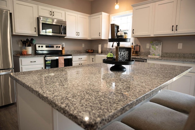 kitchen featuring light stone countertops, dark hardwood / wood-style flooring, a center island, stainless steel appliances, and white cabinetry