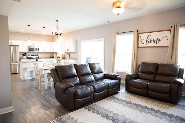 living room with dark wood-type flooring, sink, and ceiling fan with notable chandelier