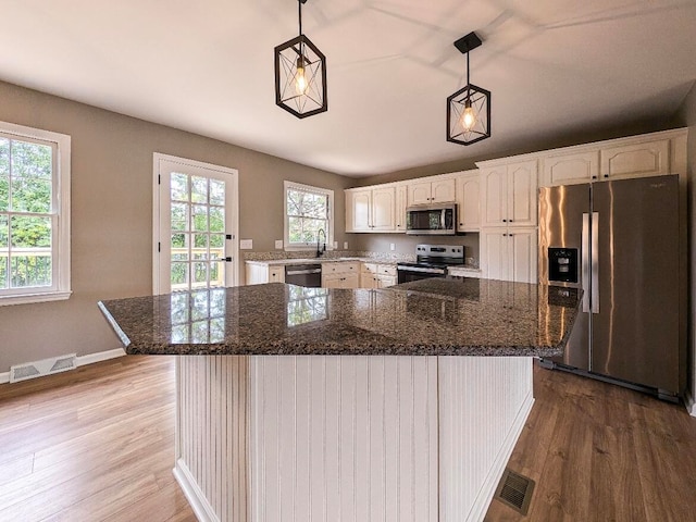 kitchen with pendant lighting, light hardwood / wood-style flooring, stainless steel appliances, a kitchen island, and white cabinets