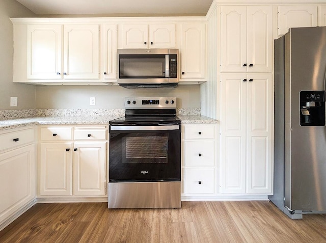 kitchen featuring light hardwood / wood-style flooring, light stone countertops, appliances with stainless steel finishes, and white cabinetry