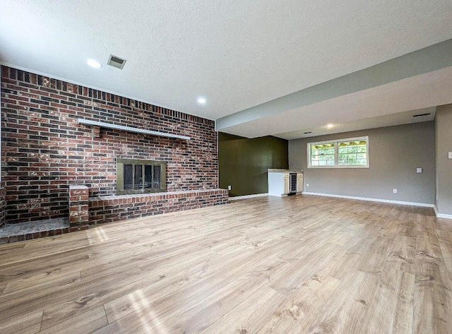 unfurnished living room featuring a fireplace, brick wall, a textured ceiling, and light hardwood / wood-style flooring