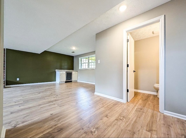 unfurnished living room featuring a textured ceiling, light hardwood / wood-style flooring, and wine cooler