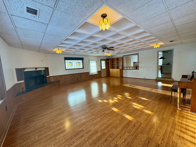 unfurnished living room with wood-type flooring, wooden walls, a paneled ceiling, and ceiling fan