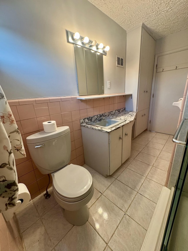 bathroom with tile walls, vanity, toilet, tile patterned floors, and a textured ceiling