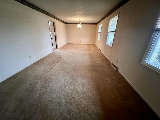 carpeted spare room featuring visible vents, baseboards, a textured ceiling, and crown molding