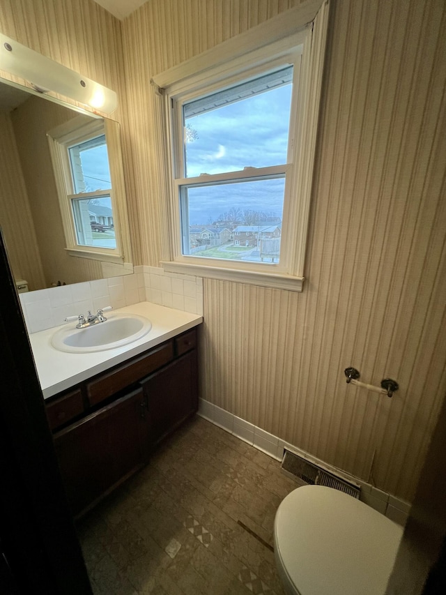 bathroom featuring vanity, visible vents, baseboards, wallpapered walls, and toilet