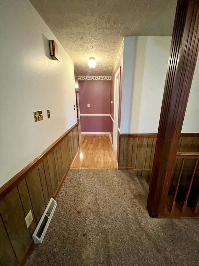 corridor featuring visible vents, a textured ceiling, wood walls, and wainscoting