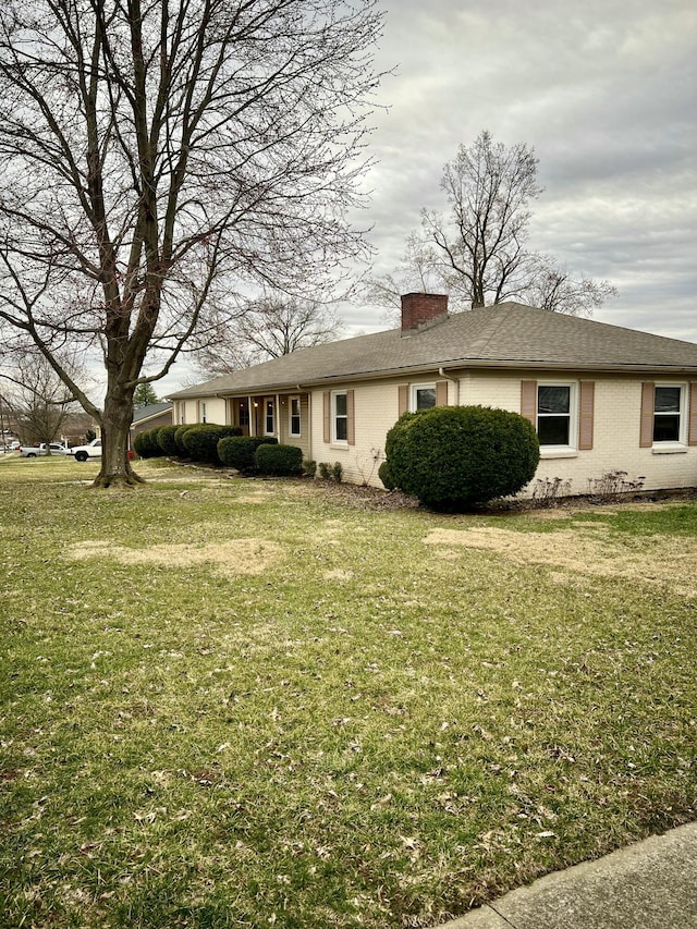 exterior space with brick siding, a chimney, and a front lawn