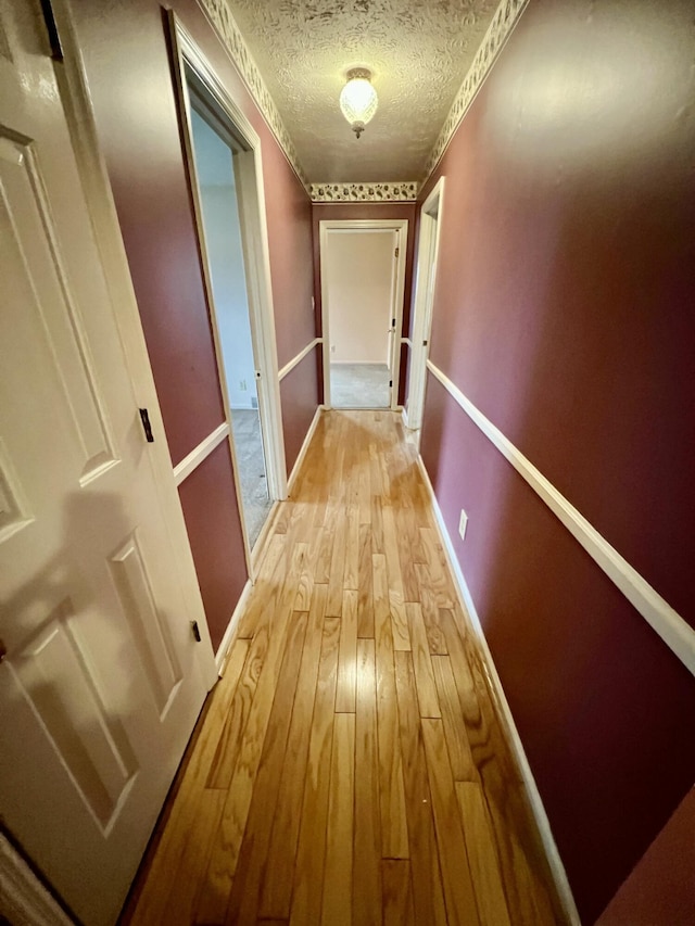 corridor featuring light wood-style floors, baseboards, and a textured ceiling