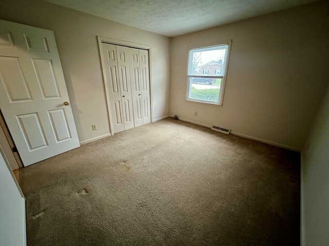 unfurnished bedroom featuring baseboards, visible vents, carpet floors, a closet, and a textured ceiling