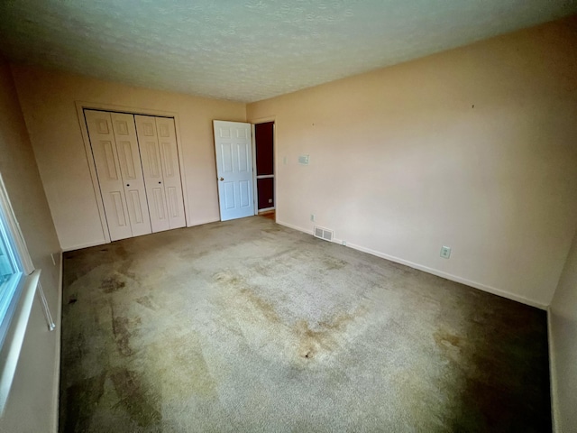 unfurnished bedroom featuring visible vents, baseboards, carpet flooring, a closet, and a textured ceiling