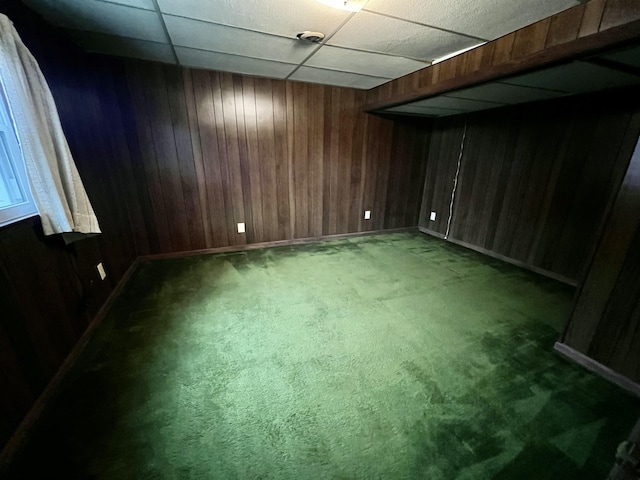 carpeted empty room with wooden walls and a drop ceiling