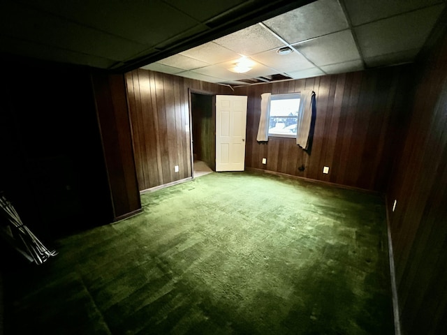 spare room featuring a drop ceiling, baseboards, wood walls, and carpet flooring