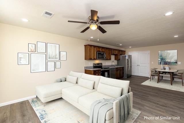 living room featuring ceiling fan, a textured ceiling, dark hardwood / wood-style floors, and sink