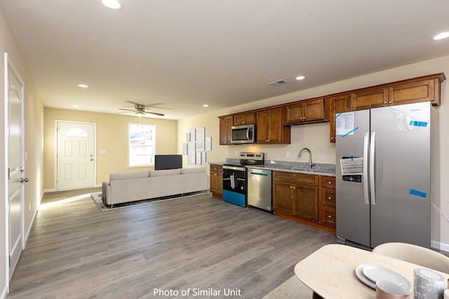 kitchen with appliances with stainless steel finishes, light stone counters, ceiling fan, light hardwood / wood-style flooring, and sink