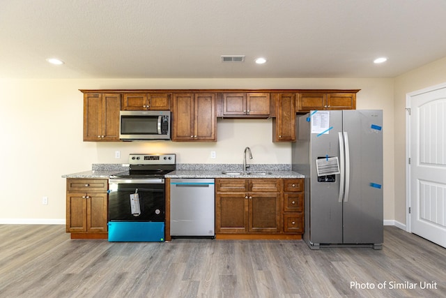 kitchen with light hardwood / wood-style floors, sink, stainless steel appliances, and light stone counters